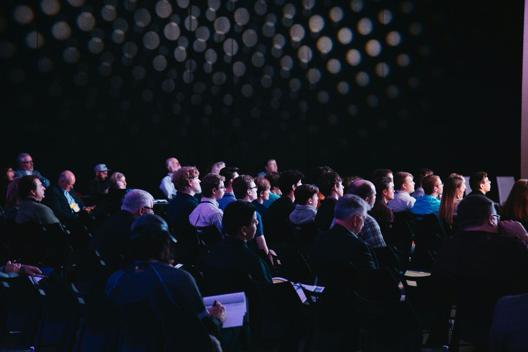 A speaker addressing a seated audience from a stage with a microphone