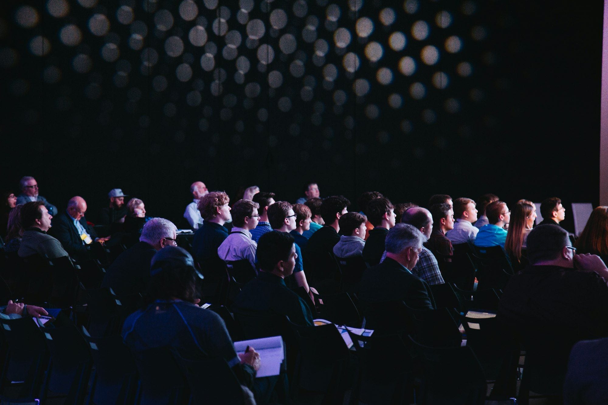 A speaker addressing a seated audience from a stage with a microphone